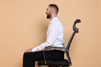 Photo of Man with good posture sitting on chair against pale orange background