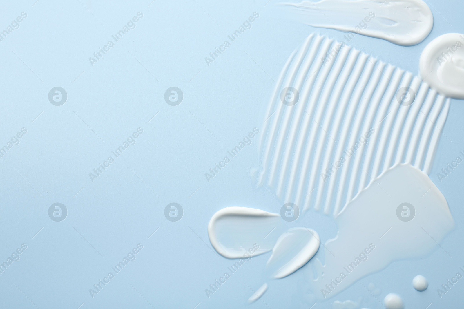 Photo of Samples of face cream on light blue background, top view. Space for text