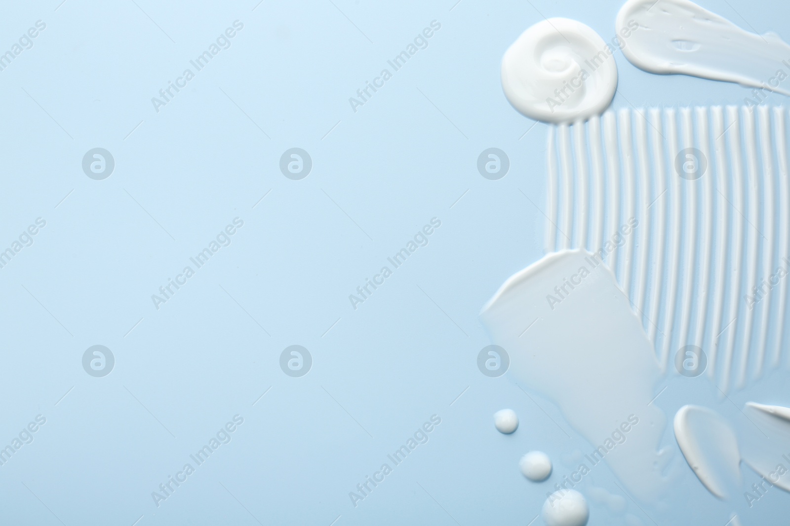 Photo of Samples of face cream on light blue background, top view. Space for text