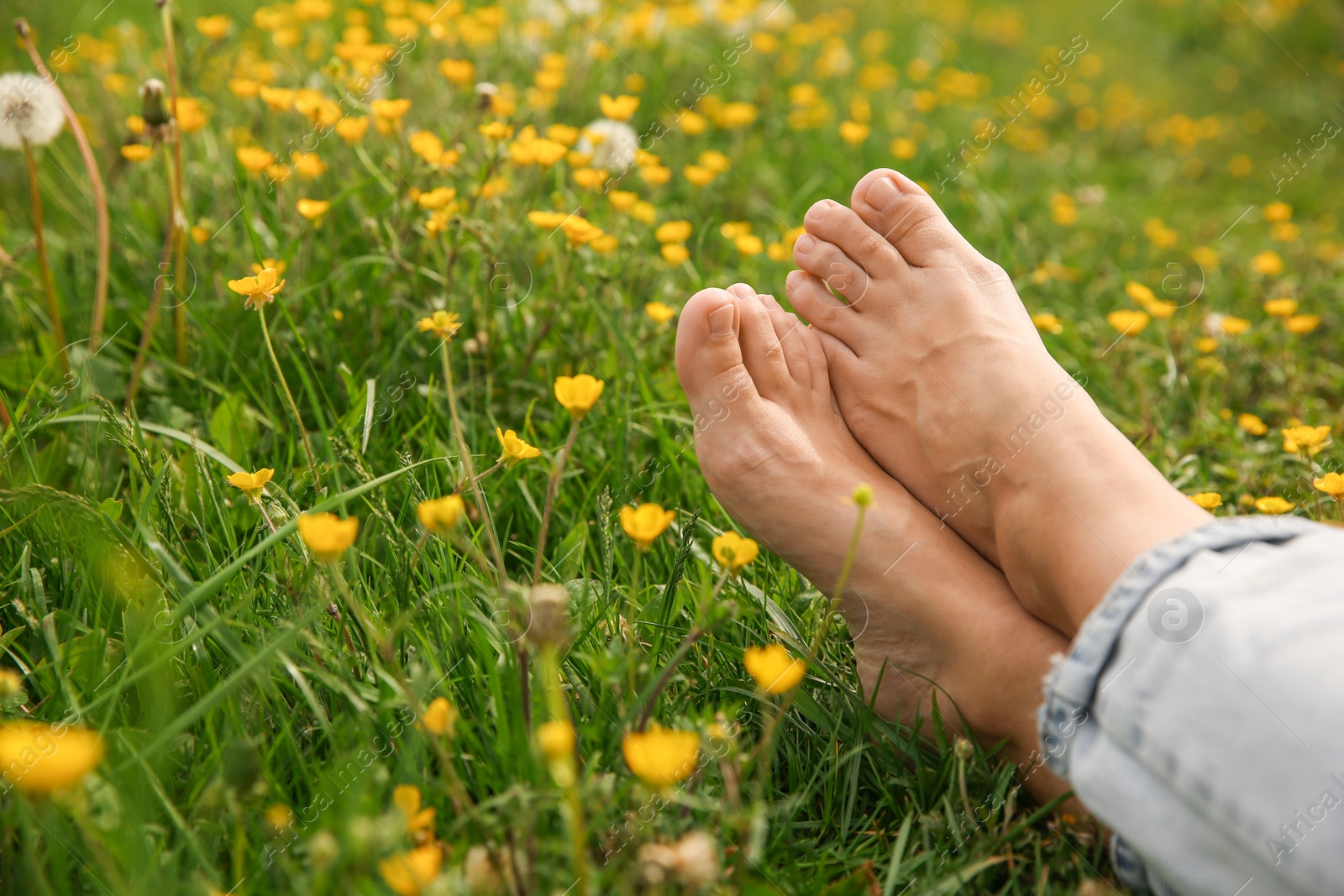 Photo of Woman sitting barefoot on green grass outdoors, closeup. Space for text