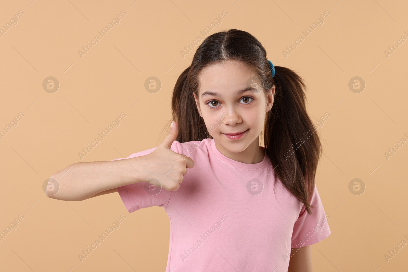 Photo of Portrait of beautiful girl showing thumbs up on beige background