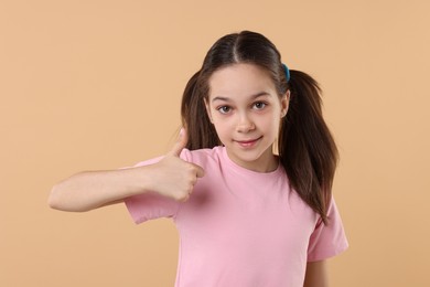 Photo of Portrait of beautiful girl showing thumbs up on beige background