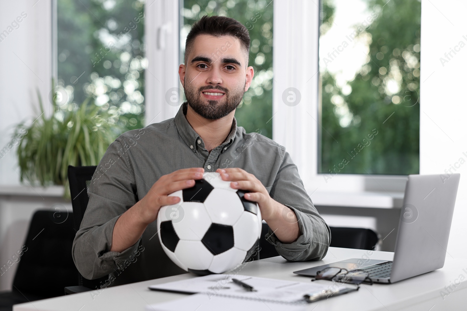 Photo of Young man with soccer ball at table in office