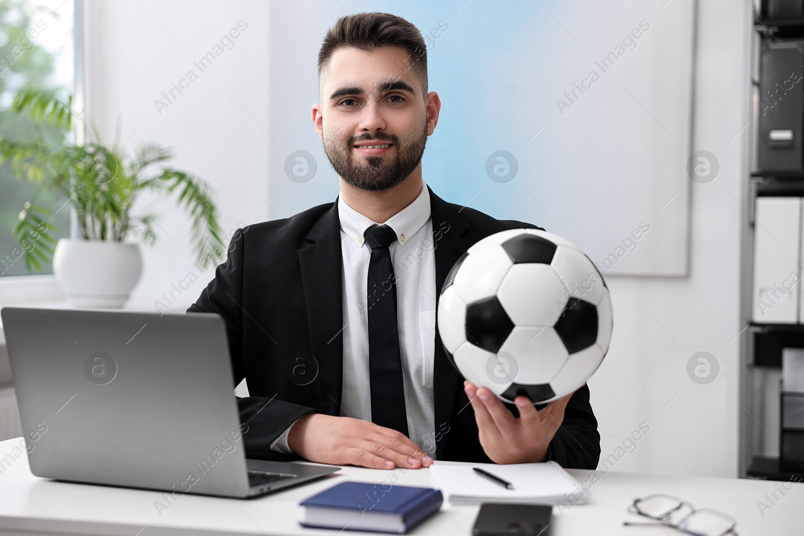 Photo of Young man with soccer ball at table in office