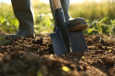 Photo of Farmer digging soil with shovel on sunny day, closeup