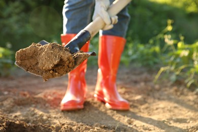 Photo of Farmer digging soil with shovel on sunny day, closeup