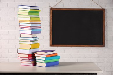 Photo of Stacks of many colorful books on white wooden table in classroom. Space for text