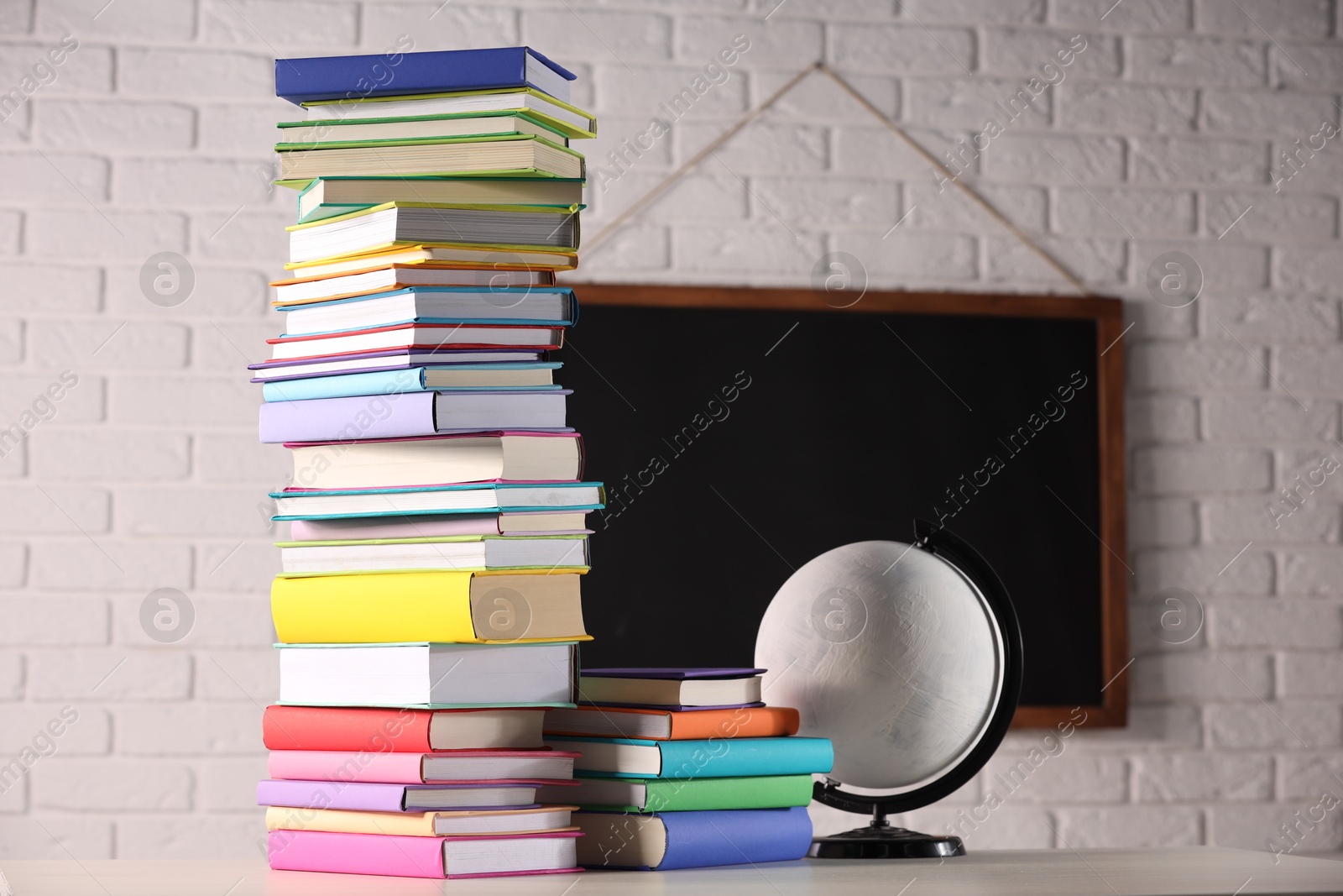 Photo of Stacks of many colorful books and globe on white table in classroom