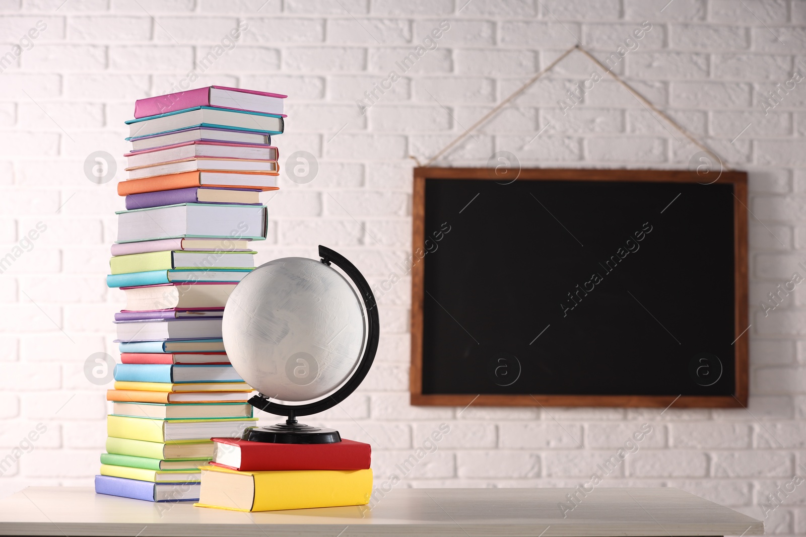 Photo of Stack of many colorful books and globe on white wooden table in classroom. Space for text