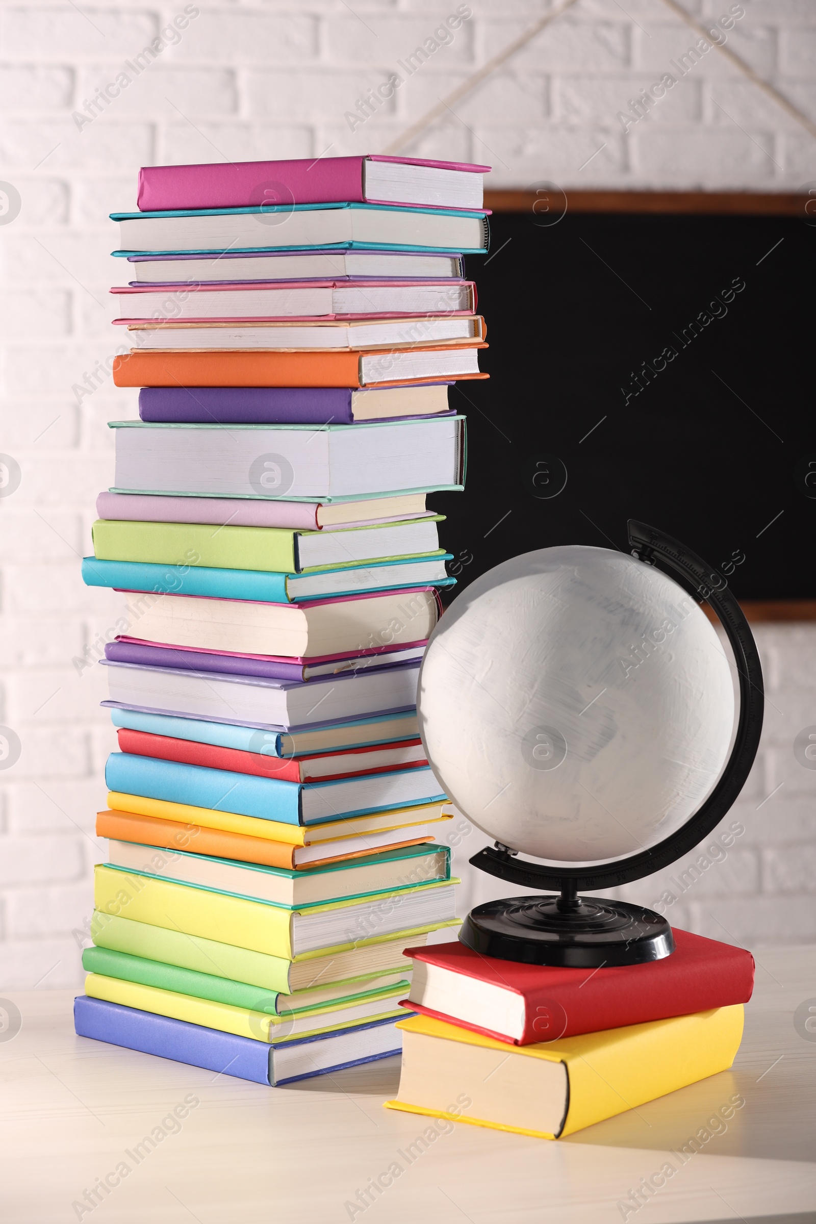 Photo of Stack of many colorful books and globe on white wooden table in classroom