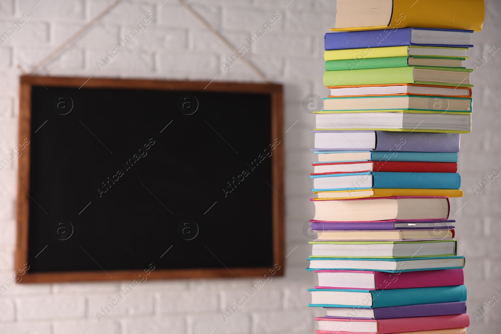 Photo of Stack of many colorful books and blackboard in classroom. Space for text