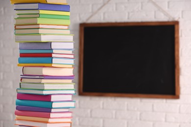 Photo of Stack of many colorful books and blackboard in classroom. Space for text