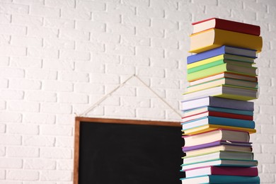 Stack of many colorful books and blackboard in classroom. Space for text