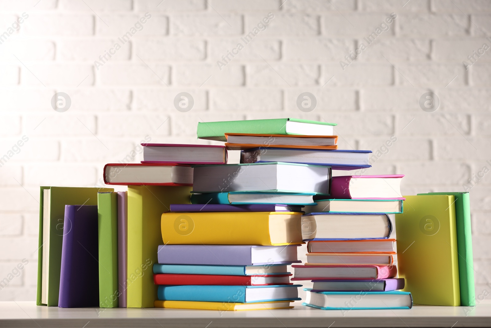 Photo of Stacks of many colorful books on white wooden table against brick wall