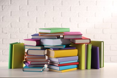 Photo of Stacks of many colorful books on white wooden table against brick wall