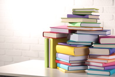 Photo of Stacks of many colorful books on white wooden table against brick wall. Space for text