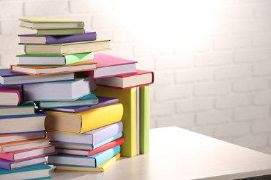 Stacks of many colorful books on white wooden table against brick wall. Space for text