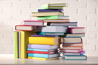 Photo of Stacks of many colorful books on white wooden table against brick wall