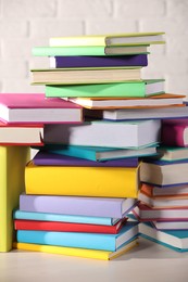 Stacks of many colorful books on white wooden table against brick wall