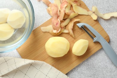 Photo of Fresh raw potatoes, peels and peeler on light grey table, top view