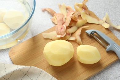 Photo of Fresh raw potatoes, peels and peeler on light grey table, top view