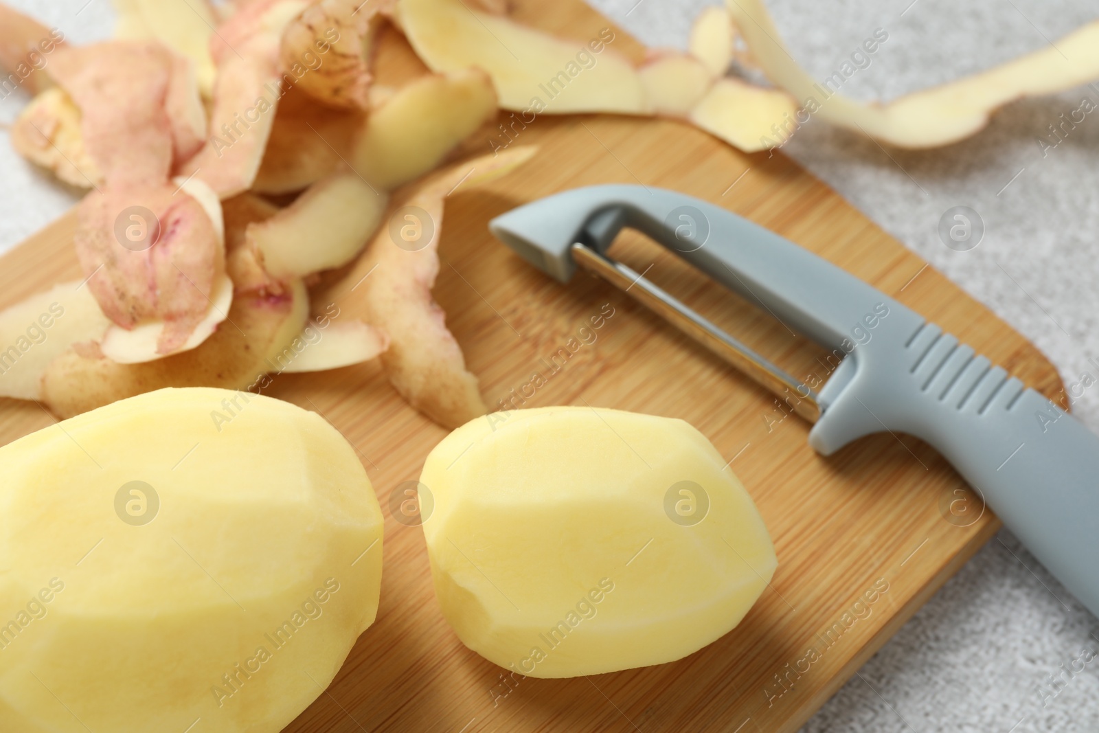 Photo of Fresh raw potatoes, peels and peeler on light grey table