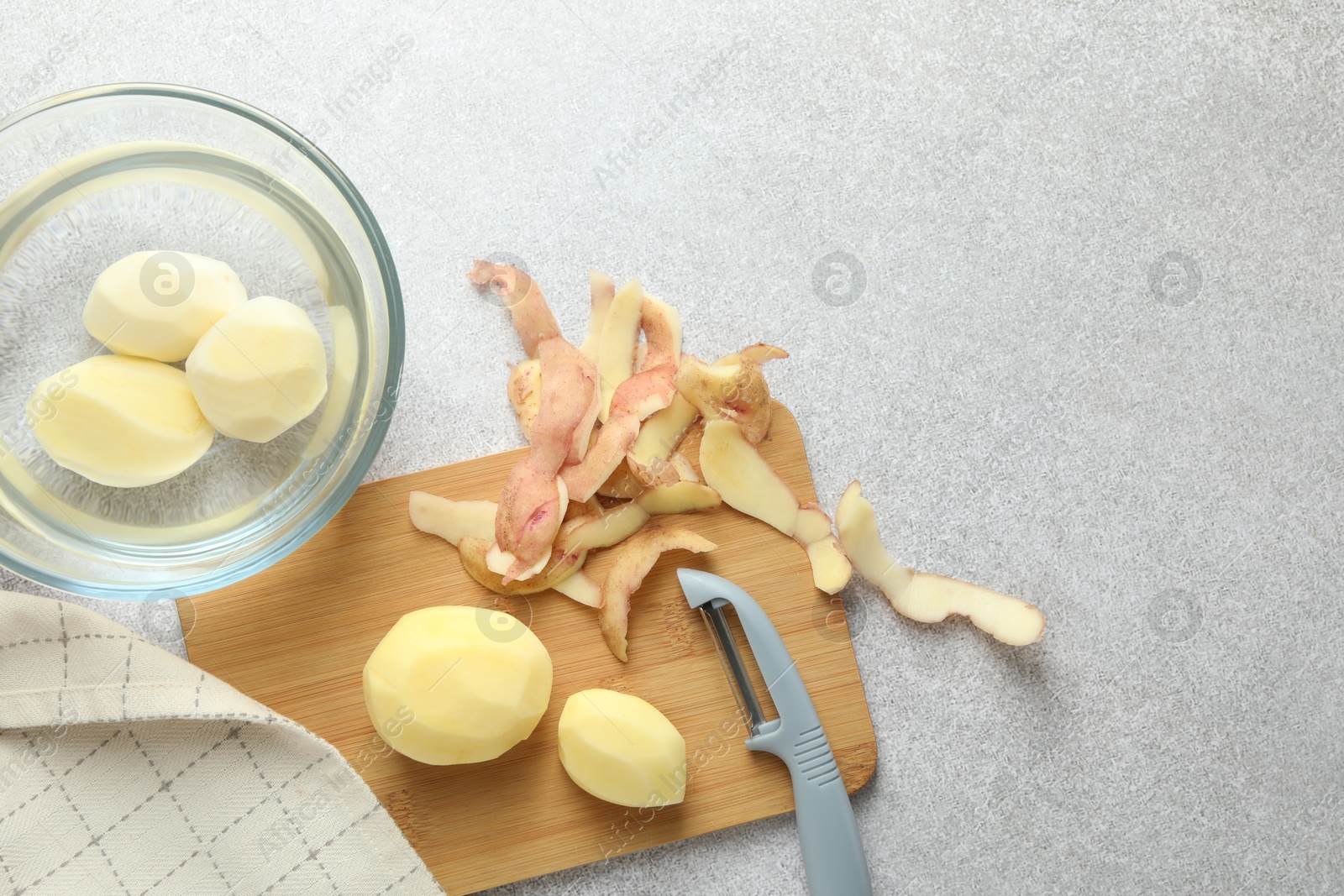 Photo of Fresh raw potatoes, peels and peeler on light grey table, top view. Space for text