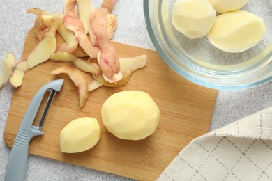 Photo of Fresh raw potatoes, peels and peeler on light grey table, top view