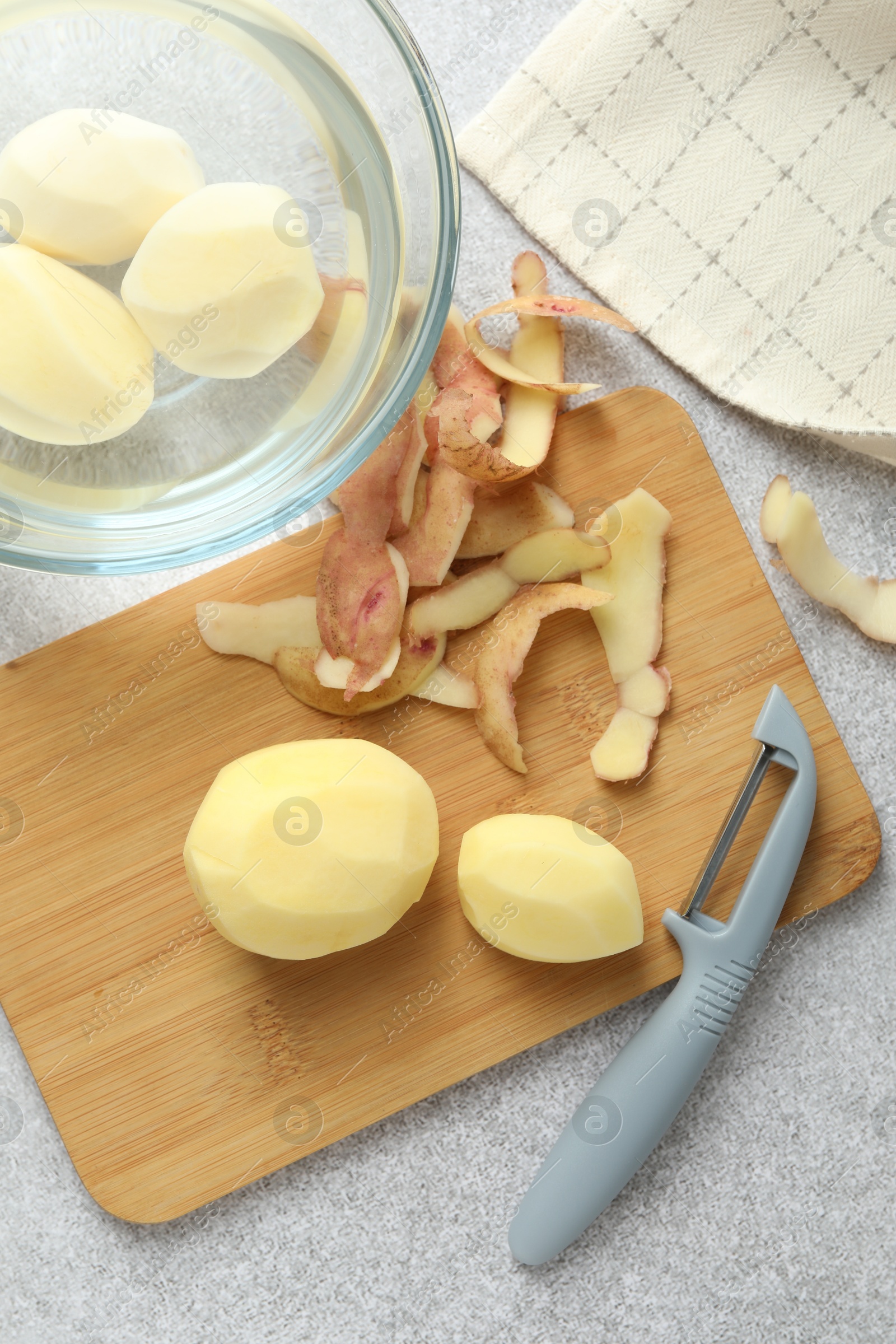 Photo of Fresh raw potatoes, peels and peeler on light grey table, top view