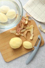 Photo of Fresh raw potatoes, peels and peeler on light grey table, top view