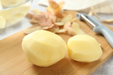 Photo of Fresh raw potatoes, peels and peeler on table, closeup