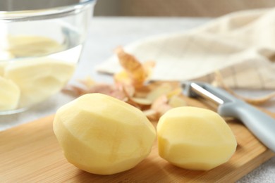 Fresh raw potatoes, peels and peeler on table, closeup