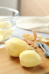 Fresh raw potatoes, peels and peeler on table