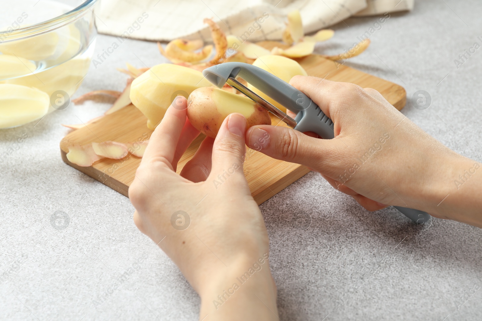 Photo of Woman peeling fresh potato with peeler at light grey table, closeup