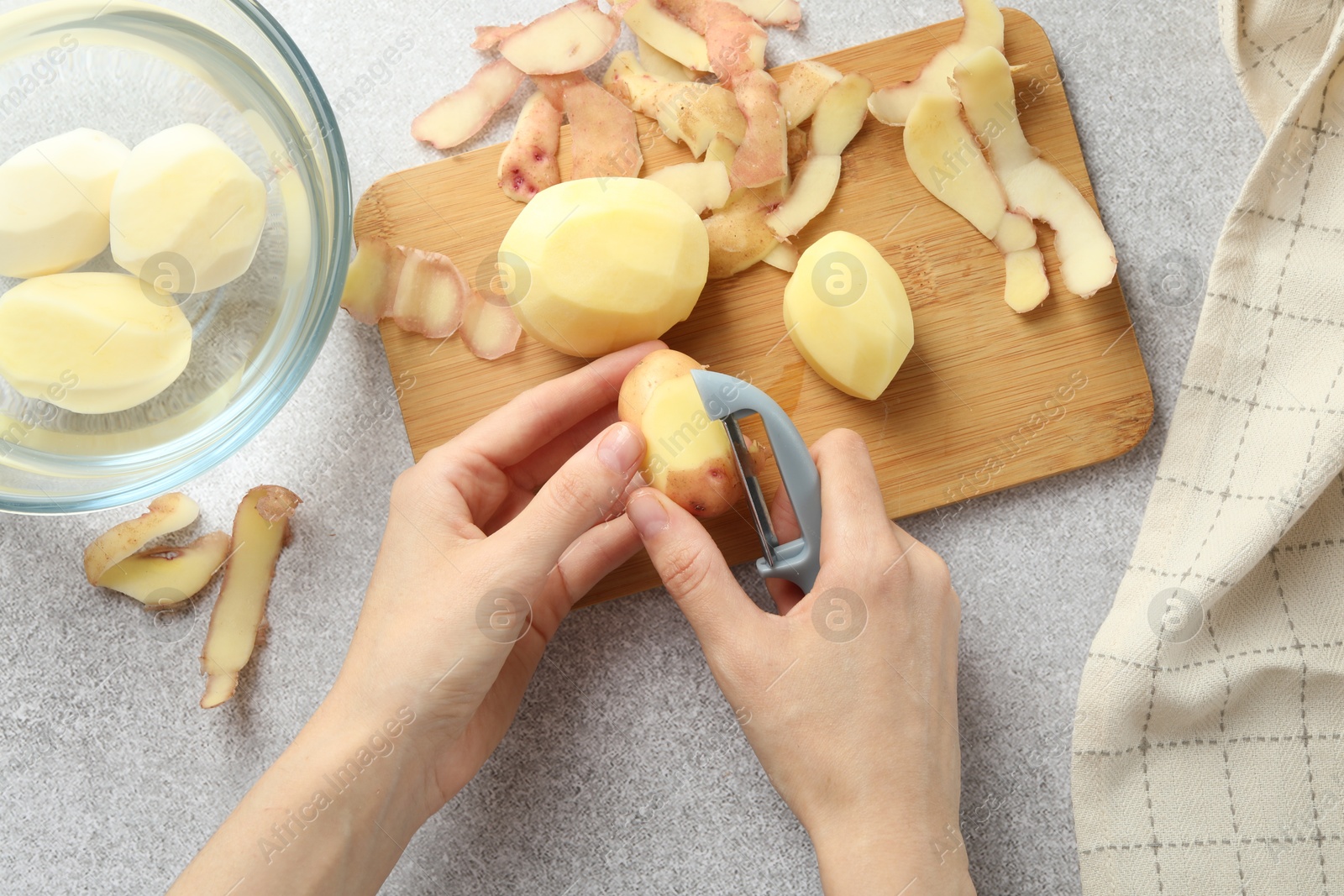 Photo of Woman peeling fresh potato with peeler at light grey table, top view