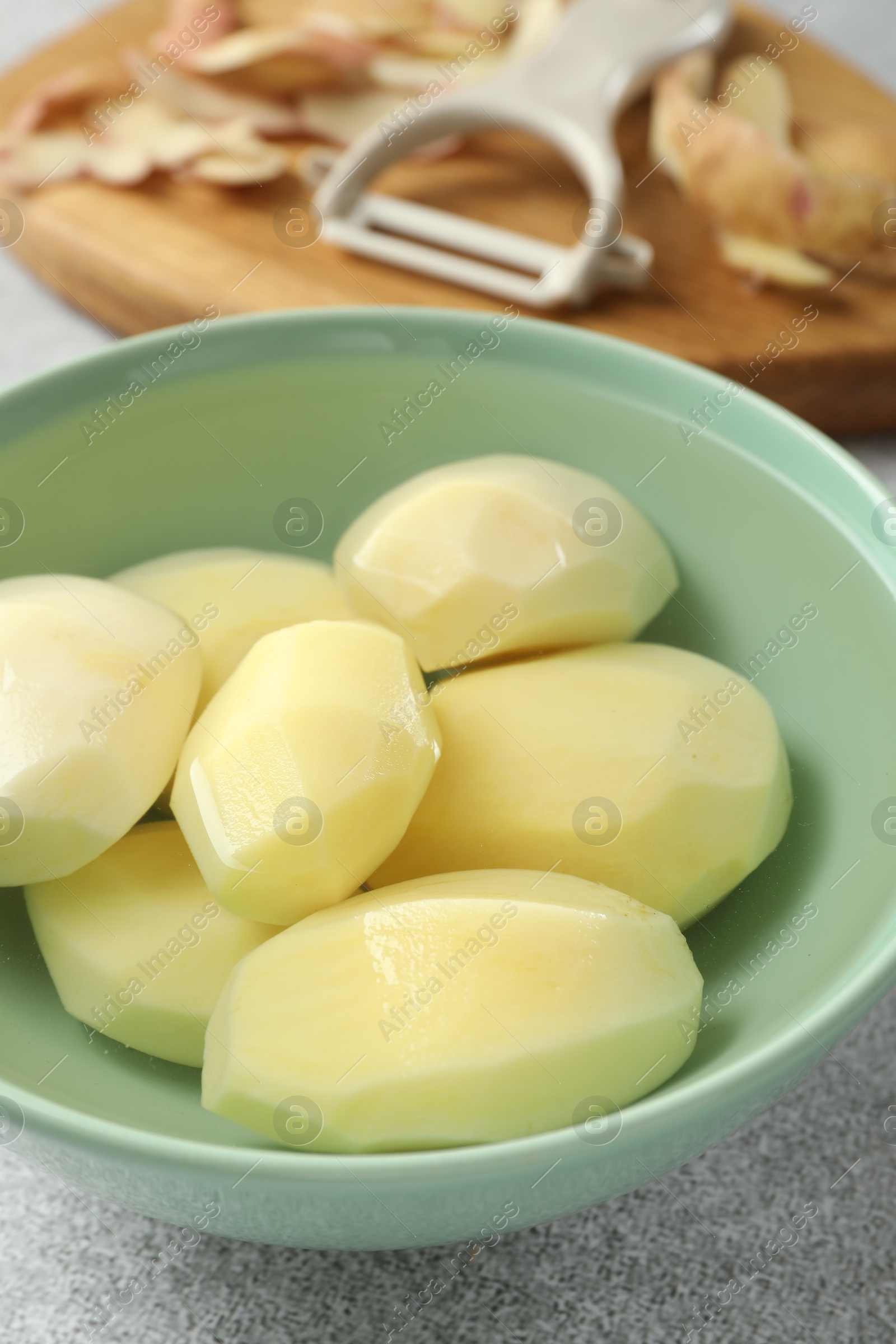 Photo of Fresh raw potatoes in bowl on light grey table, closeup