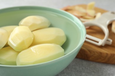 Photo of Fresh raw potatoes in bowl on light grey table, closeup