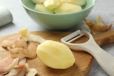 Photo of Fresh raw potatoes, peels and peeler on light grey table