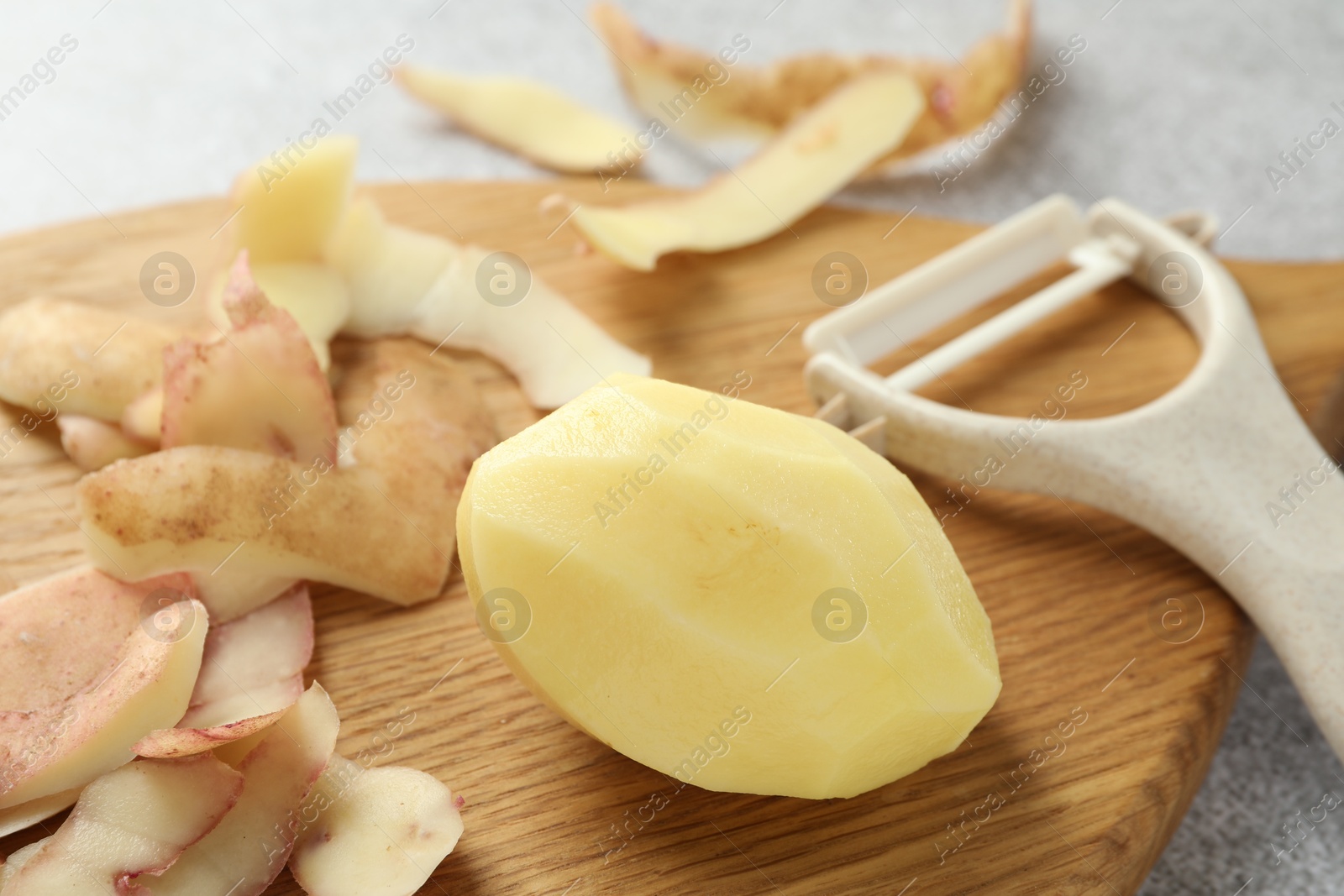 Photo of Fresh raw potato, peels and peeler on table, closeup