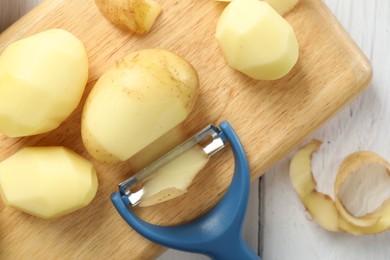 Photo of Fresh raw potatoes, peels and peeler on white wooden table, top view