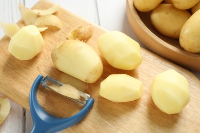 Photo of Fresh raw potatoes, peels and peeler on white wooden table