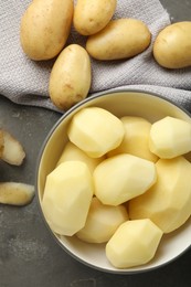 Photo of Fresh raw potatoes and peels on grey table, top view