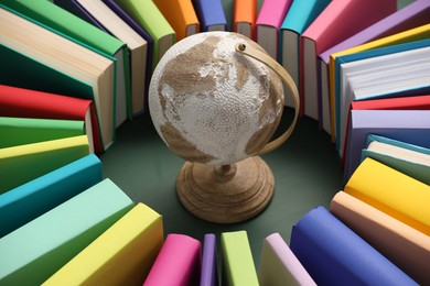 Globe surrounded by many colorful books on green background, closeup