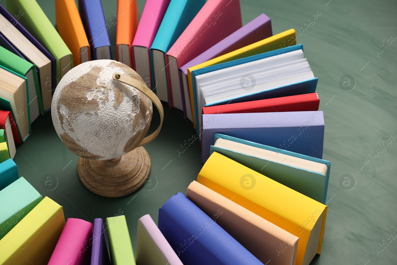 Photo of Globe surrounded by many colorful books on green background, closeup