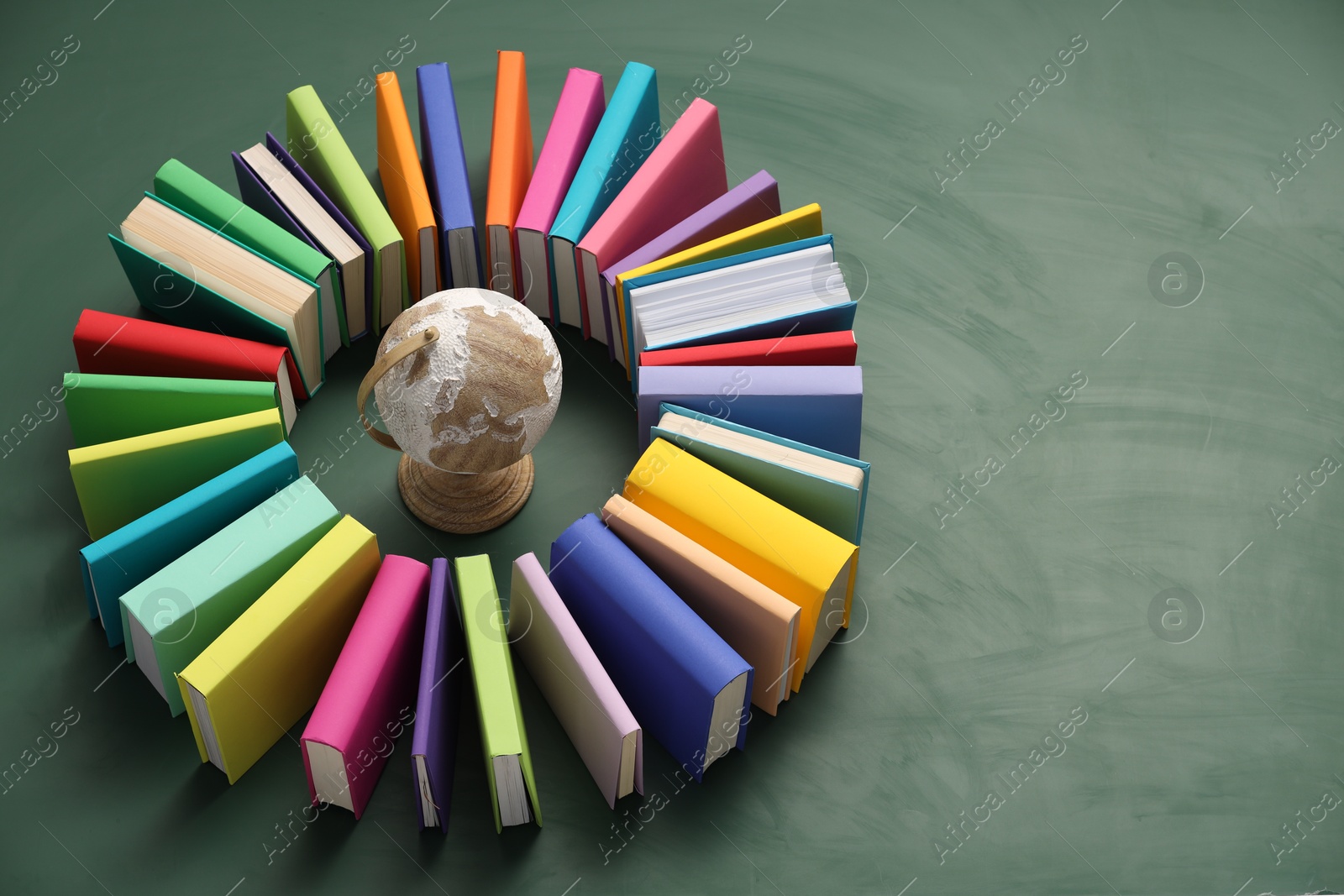 Photo of Globe surrounded by many colorful books on green background. Space for text