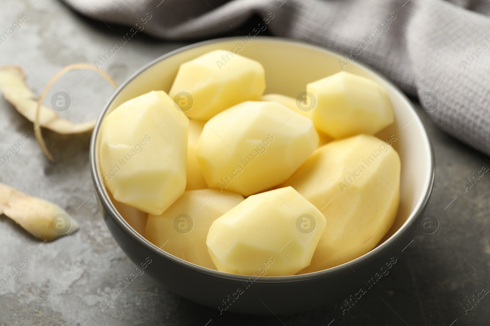 Photo of Fresh raw potatoes in bowl and peels on grey table, closeup