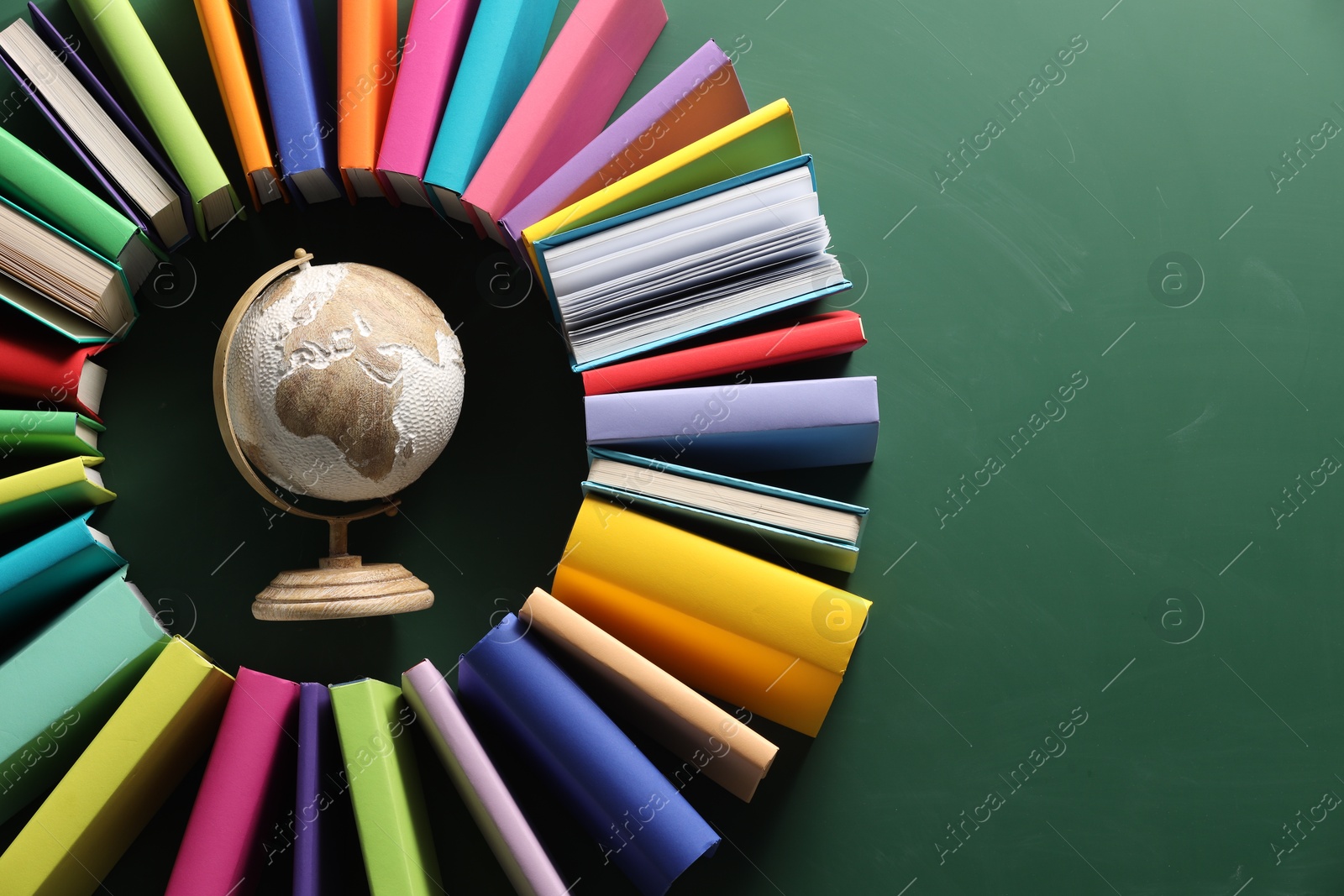 Photo of Globe surrounded by many colorful books on green background, flat lay. Space for text