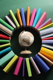 Photo of Globe surrounded by many colorful books on green background, flat lay