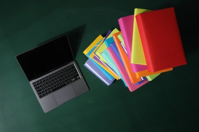 Photo of Stack of many colorful books and laptop on green background, flat lay