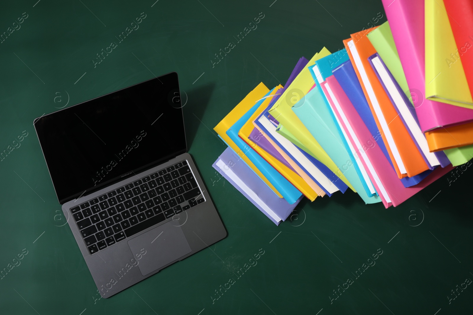 Photo of Stack of many colorful books and laptop on green background, above view